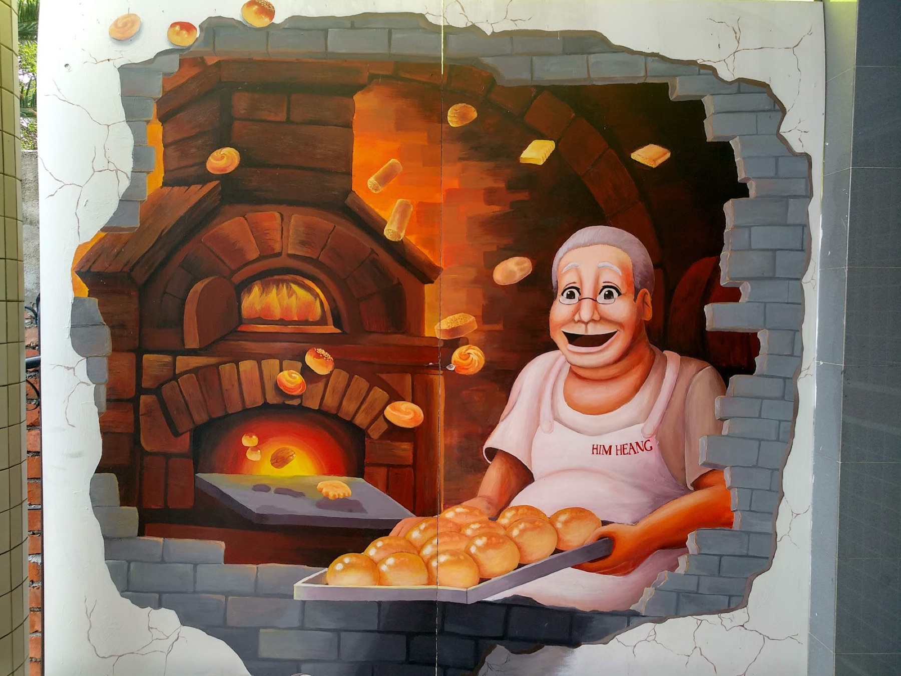 Hand-painted mural on the Him Heang wall — a smiling baker pulling a tray of golden pastries from a brick oven